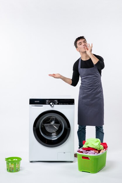 Front view of young male with dirty clothes and washer on white wall