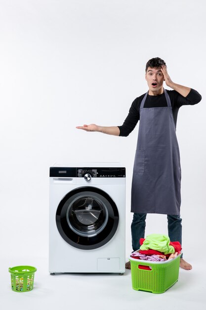 Front view of young male with dirty clothes and washer on white wall