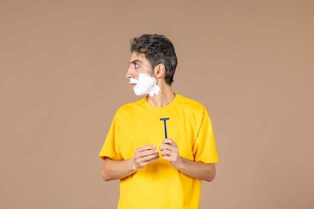 front view young male with foam on his face preparing to shave on pink background