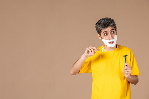 front view young male with foam on his face preparing to shave on pink background