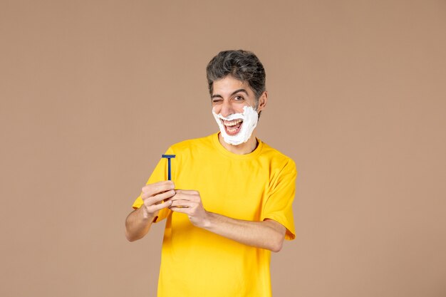 front view young male with foam on his face and razor in his hands on pink background