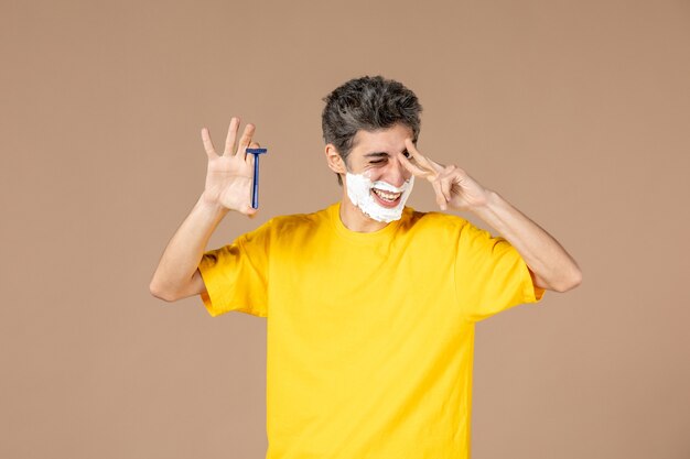 front view young male with foam on his face and razor in his hands on pink background