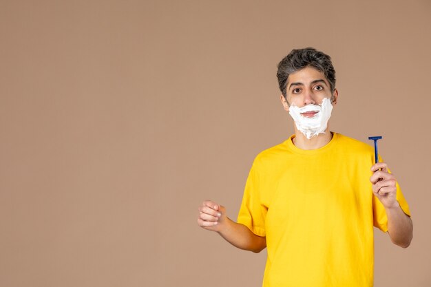 front view young male with foam on his face and razor shaving on pink background