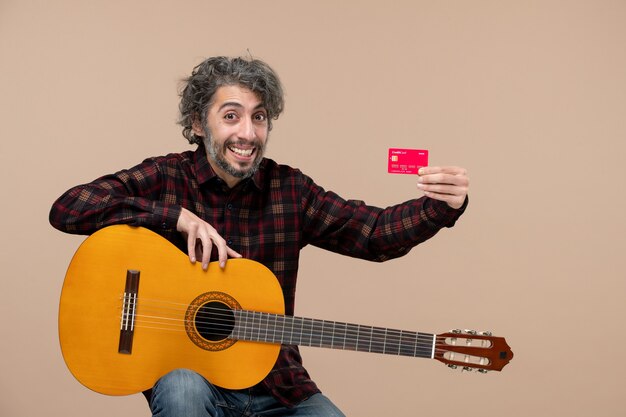 Вид спереди молодого мужчины с гитарой, держащего красную банковскую карту на розовой стене