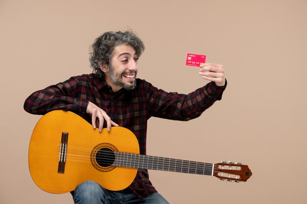 ピンクの壁に赤い銀行カードを保持しているギターを持つ若い男性の正面図