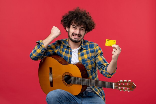 Front view young male with guitar holding yellow bank card on red wall color performance applause musician concert