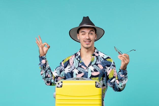 Front view of young male with his yellow bag preparing for long trip on the blue wall