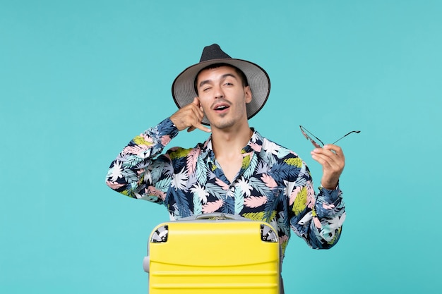 Front view of young male with his yellow bag preparing for long trip on light blue wall