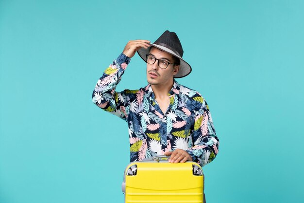 Front view of young male with his yellow bag preparing for trip on blue surface