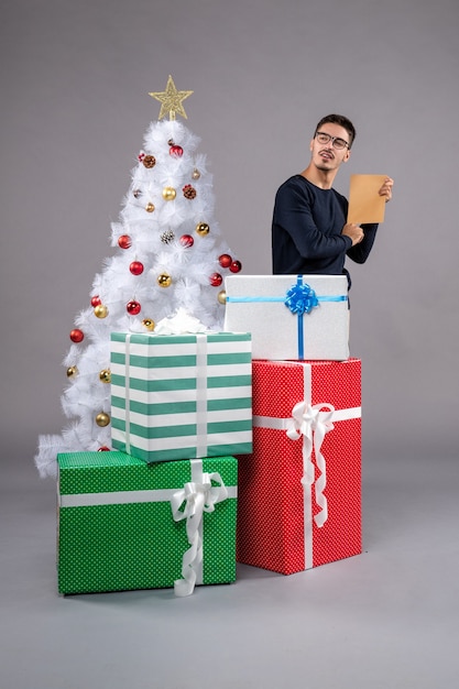 Вид спереди молодой самец с праздничными подарками на сером полу новогодний человеческий подарок на рождество
