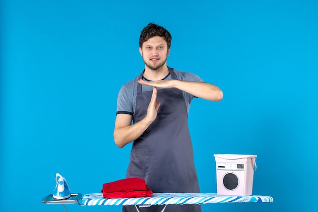 Front view young male with ironing board on the blue background housework color iron laundry washing machine man cleaning