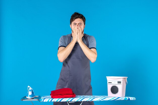 Front view young male with ironing board on a blue surface