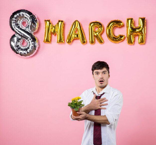 Front view young male with little flower in pot on his head with march decoration on pink background man womens day equality present colors party