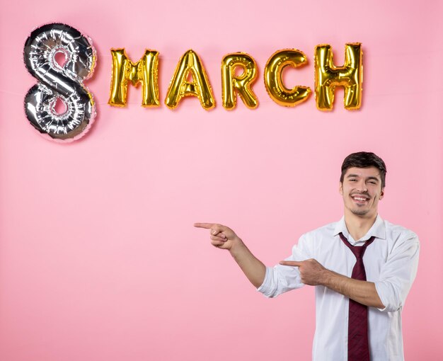 Вид спереди молодой мужчина с украшением марта на розовом фоне мужчина представляет женский женский день цвет партии брак