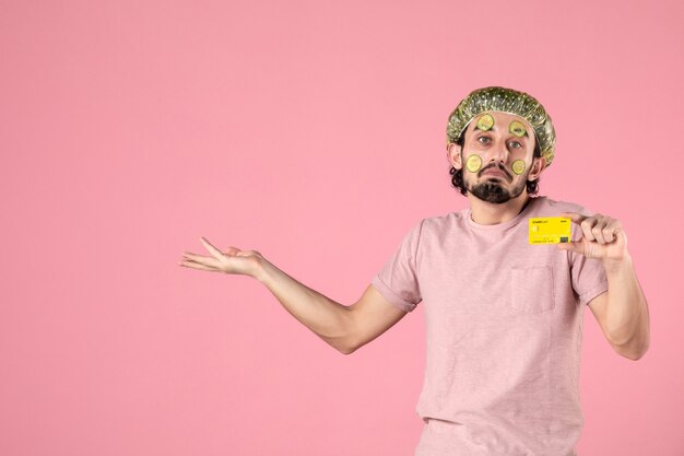 front view young male with mask on his face holding bank card on pink background