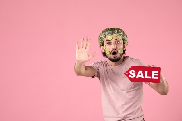 front view young male with mask on his face holding sale nameplate on pink background