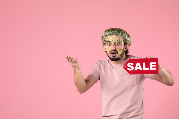 front view young male with mask on his face holding sale nameplate on pink background