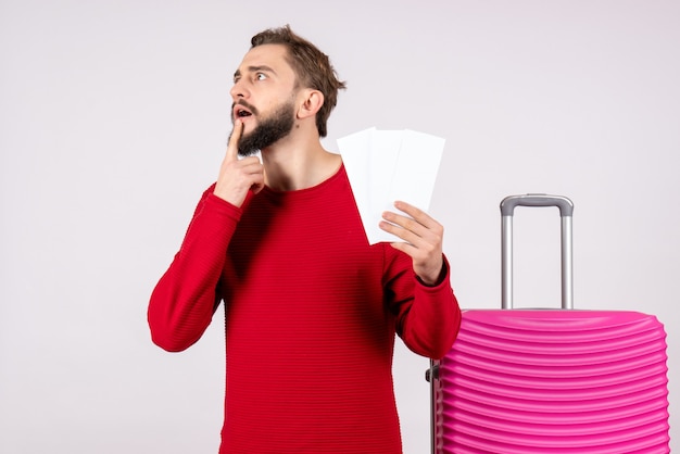 Front view young male with pink bag and holding plane tickets on white wall flight trip vacation emotion photo tourist