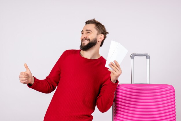ピンクのバッグと白い壁に飛行機のチケットを保持している正面図若い男性航海飛行旅行観光休暇感情写真