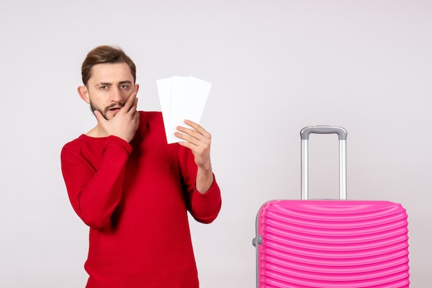 Вид спереди молодой мужчина с розовой сумкой и держит билеты на самолет на белой стене рейс рейс поездка туристический отпуск эмоция фото