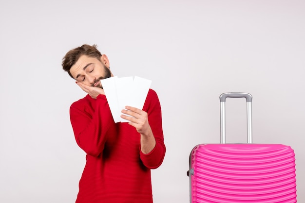 Giovane maschio di vista frontale con la borsa rosa e che tiene i biglietti che si sentono stanchi sull'emozione della foto di vacanza turistica di viaggio di volo di colore di viaggio della parete bianca