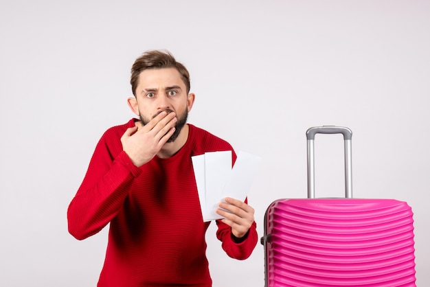 Вид спереди молодой мужчина с розовой сумкой и держит билеты на белой стене, цветная поездка, отпуск, рейс, летний турист,