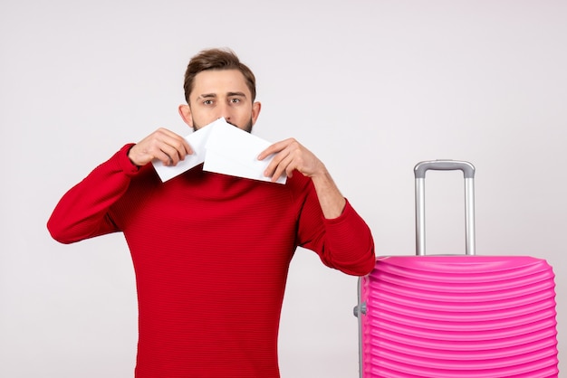 Vista frontale giovane maschio con borsa rosa e tenendo i biglietti sulla parete bianca viaggio colore viaggio vacanza turistica emozione foto