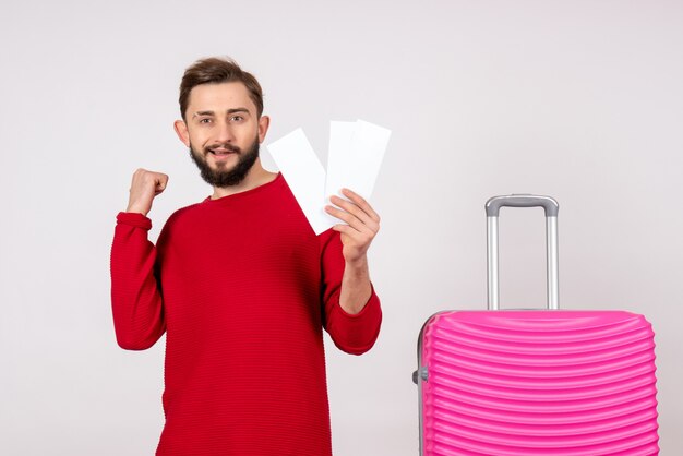 ピンクのバッグと白い壁のチケットを保持している正面図若い男性航海飛行カラー旅行観光休暇感情写真