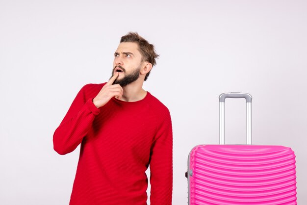 白い壁にピンクのバッグを持つ若い男性の正面図旅行写真人間の色の休暇の飛行航海