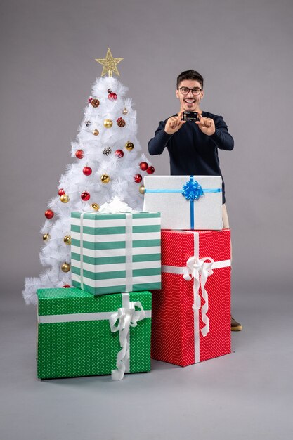 灰色の机の休日の新年のクリスマスにプレゼントと銀行カードを持つ若い男性の正面図