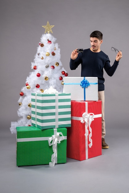 灰色の机の新年のクリスマスにプレゼントと銀行カードを持つ若い男性の正面図