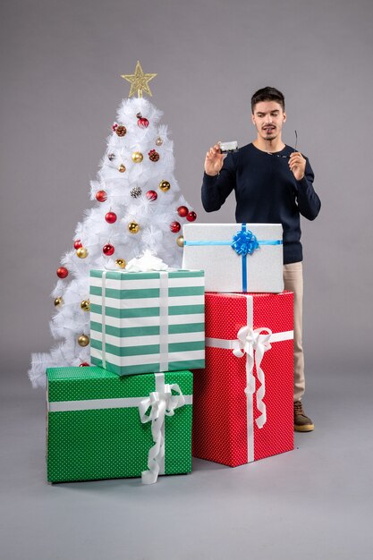 Front view young male with presents and bank card on grey floor new year christmas