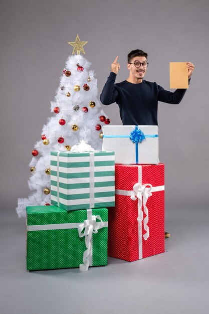 Front view young male with presents and envelop on light desk holiday new year christmas
