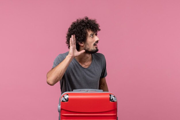 Front view young male with red bag preparing for trip listening on pink space