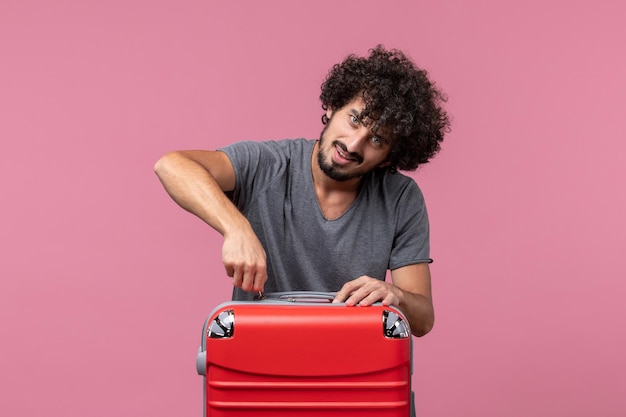 ピンクのスペースで旅行の準備をしている赤いバッグを持つ若い男性の正面図