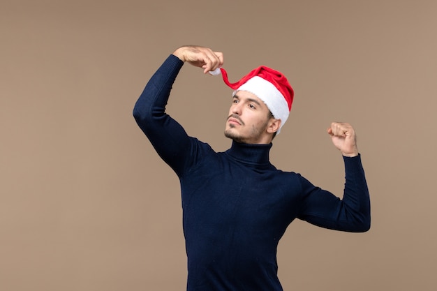 茶色の机の休日のクリスマスイブに赤いクリスマスキャップを持つ若い男性の正面図