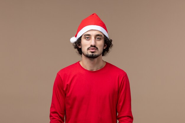 茶色の背景の感情の休日のクリスマスに赤いクリスマスマントと正面図若い男性
