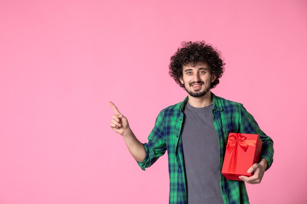 Front view of young male with red package on light pink wall