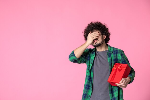 Front view of young male with red package on light pink wall