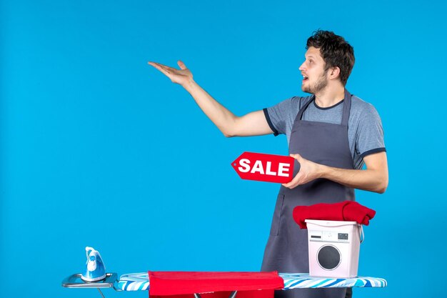 Free photo front view young male with red sale writing in his hands on the blue background housework laundry iron shopping washing machine cleaning