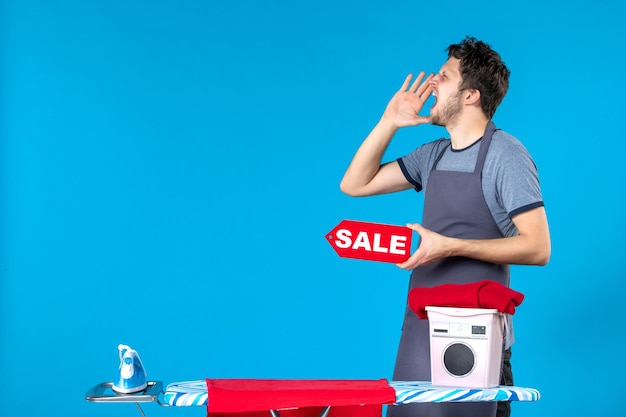 Free photo front view young male with red sale writing in his hands on blue background housework laundry shopping washing machine cleaning iron