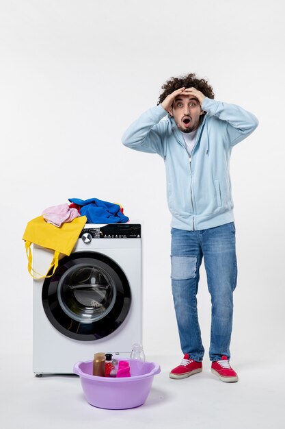 Front view of young male with washer and dirty clothes on a white wall