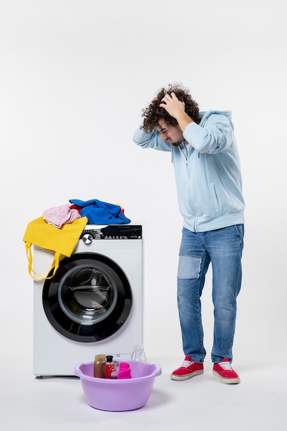 Front view of young male with washer and dirty clothes on a white wall