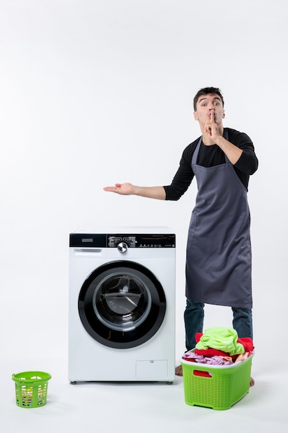 Front view of young male with washer and dirty clothes on the white wall