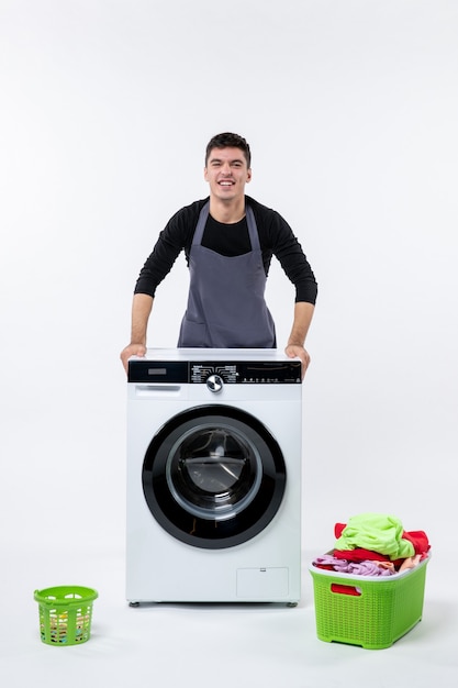 Front view of young male with washer and dirty clothes on the white wall