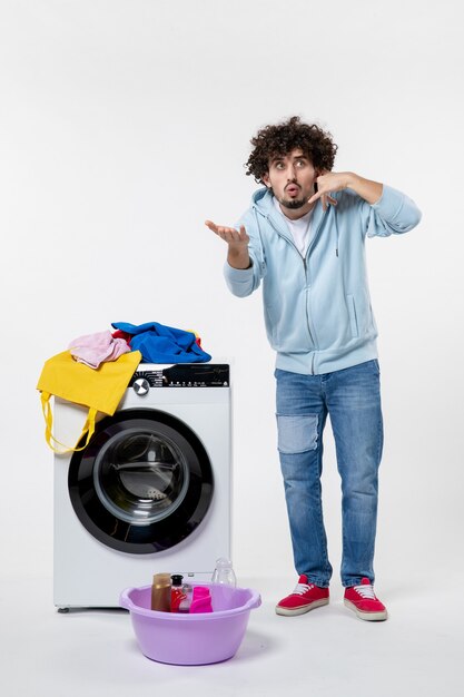 Front view of young male with washer and dirty clothes on the white wall