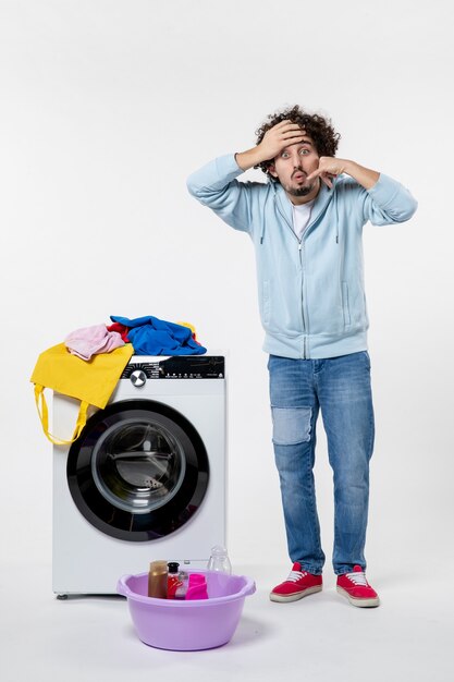 Front view of young male with washer and dirty clothes on the white wall