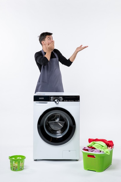 Front view of young male with washer and dirty clothes on the white wall