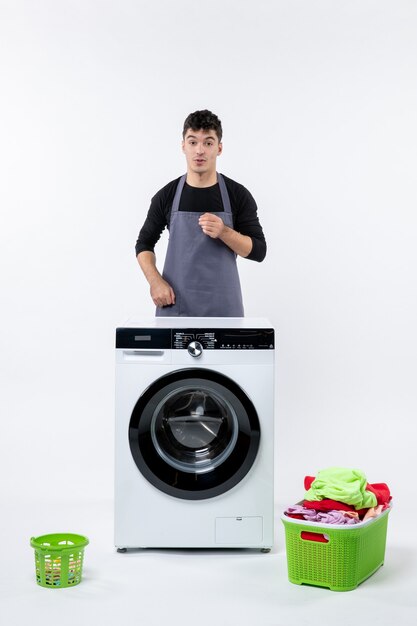 Front view of young male with washer and dirty clothes on white wall