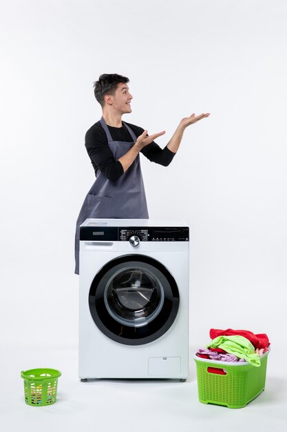 Front view of young male with washer and dirty clothes on white wall